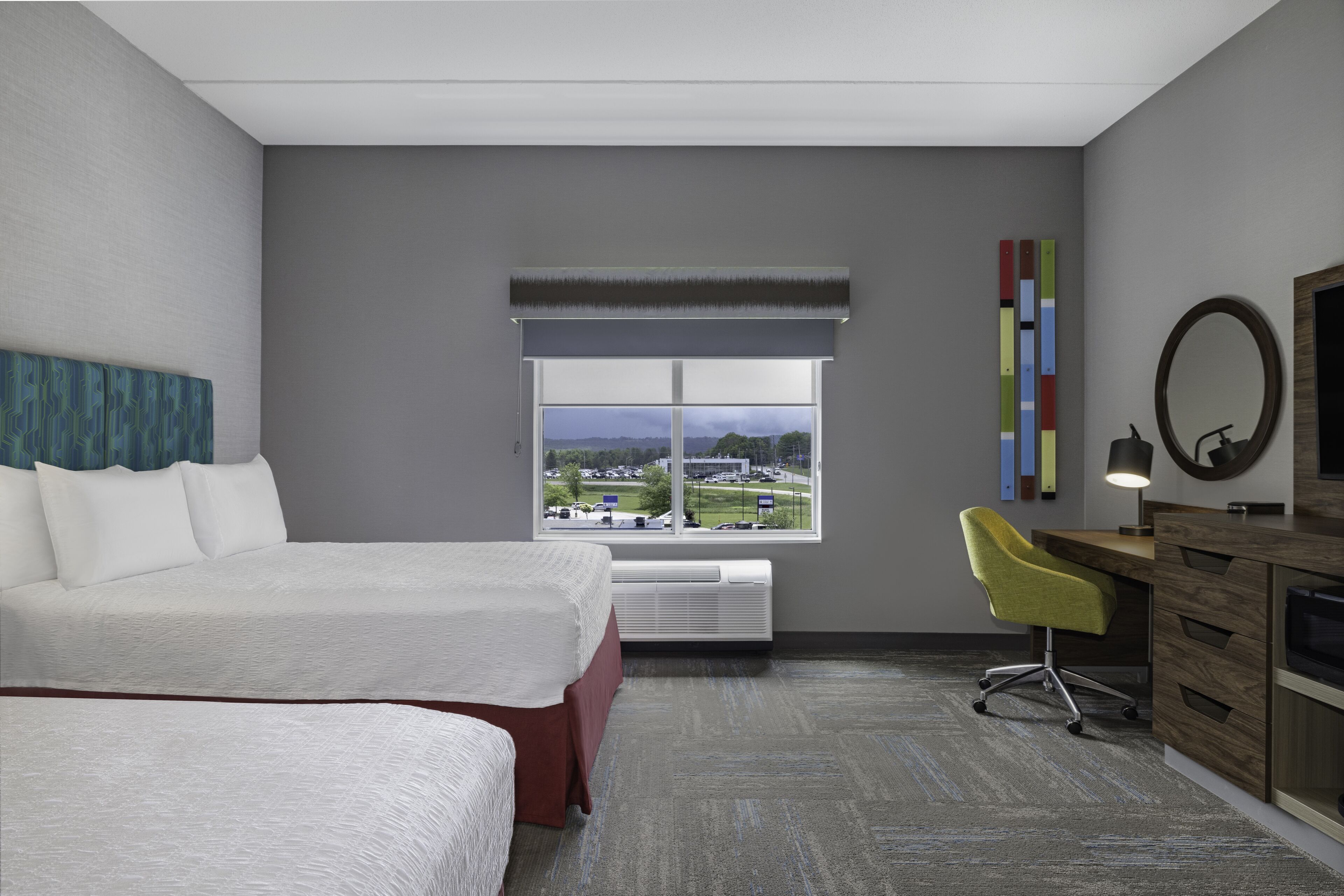 A hotel room with a large bed, a desk with a chair, a window with a view, and a mirror.