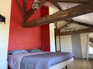 Ein Schlafzimmer mit Bett, Holzbalken, einer roten Wand und einer Chandelier.