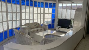 A sunlit room with a curved white counter, wicker furniture, a flat-screen TV, and large windows with blue-tinted glass. - Beautiful Villa La Concepcion (Cuernavaca)