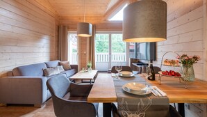 Un accogliente interno di una baita in legno, con un tavolo da pranzo per due persone, un divano e una TV montata a parete.