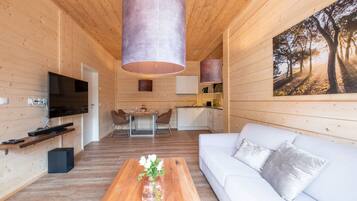 L’intérieur d’une maison en rondins moderne présente un coin repas en bois, un salon avec un canapé et une table basse, et une cuisine avec des meubles blancs.