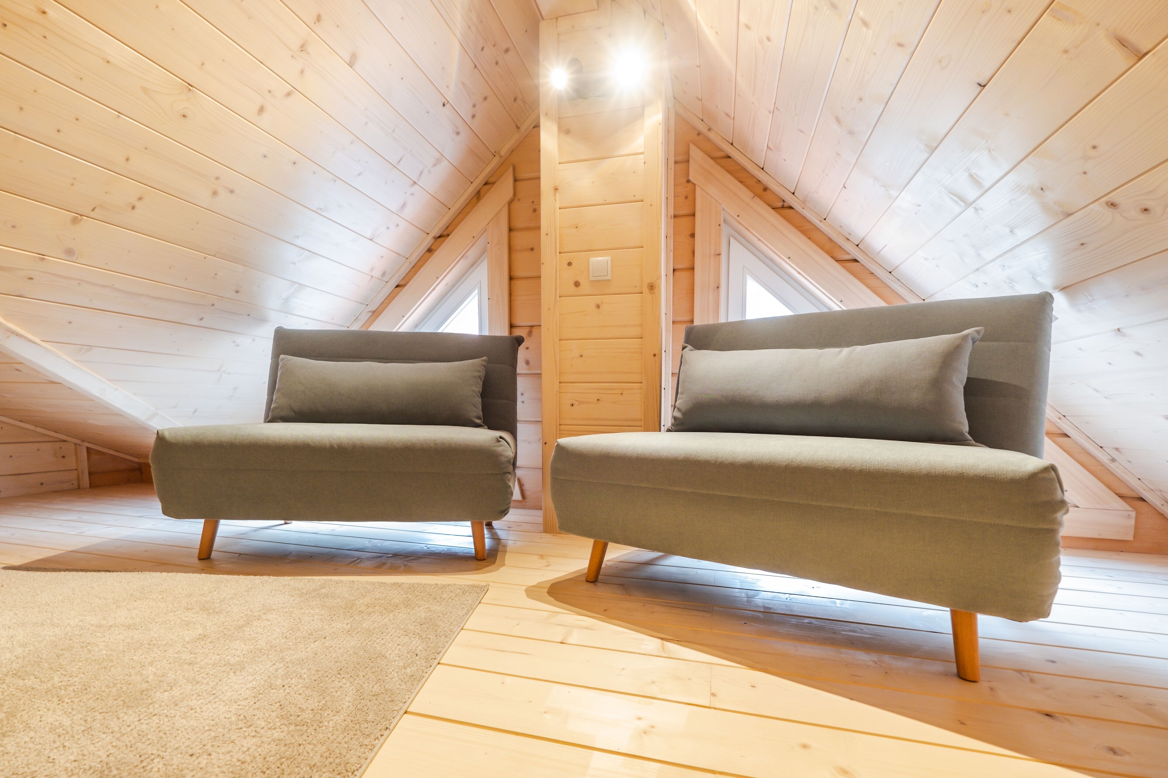 Une pièce mansardée chaleureuse, avec deux fauteuils verts, un plancher en bois et un plafond en pente laissant entrer la lumière naturelle par les fenêtres.
