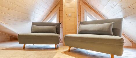 Une pièce mansardée chaleureuse, avec deux fauteuils verts, un plancher en bois et un plafond en pente laissant entrer la lumière naturelle par les fenêtres.