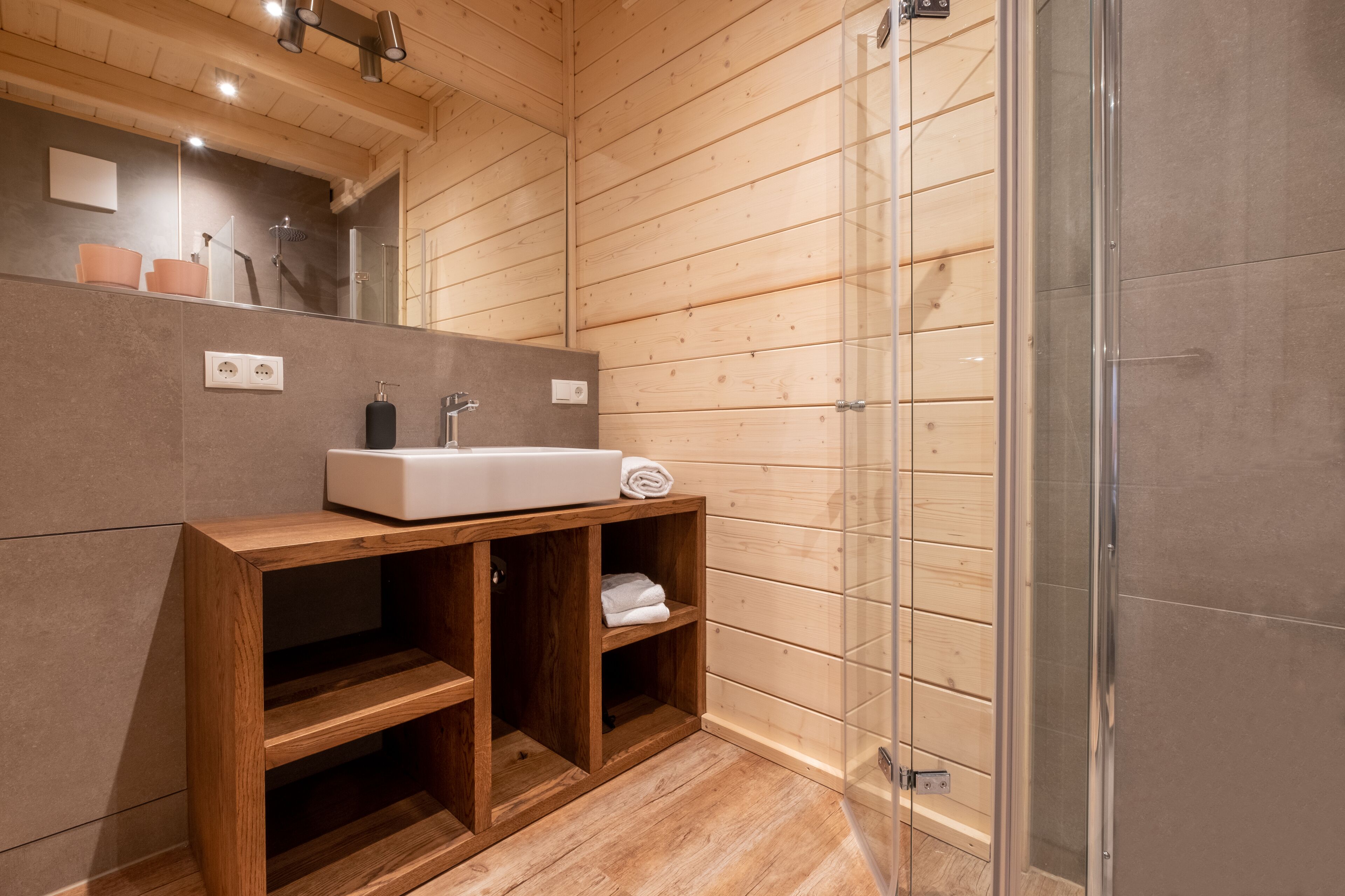 A wooden cabin bathroom with a large mirror, a sink, and a glass shower enclosure.