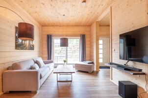 Interior de uma cabana de madeira com sofá, mesa de centro, televisão e parede de pedra.