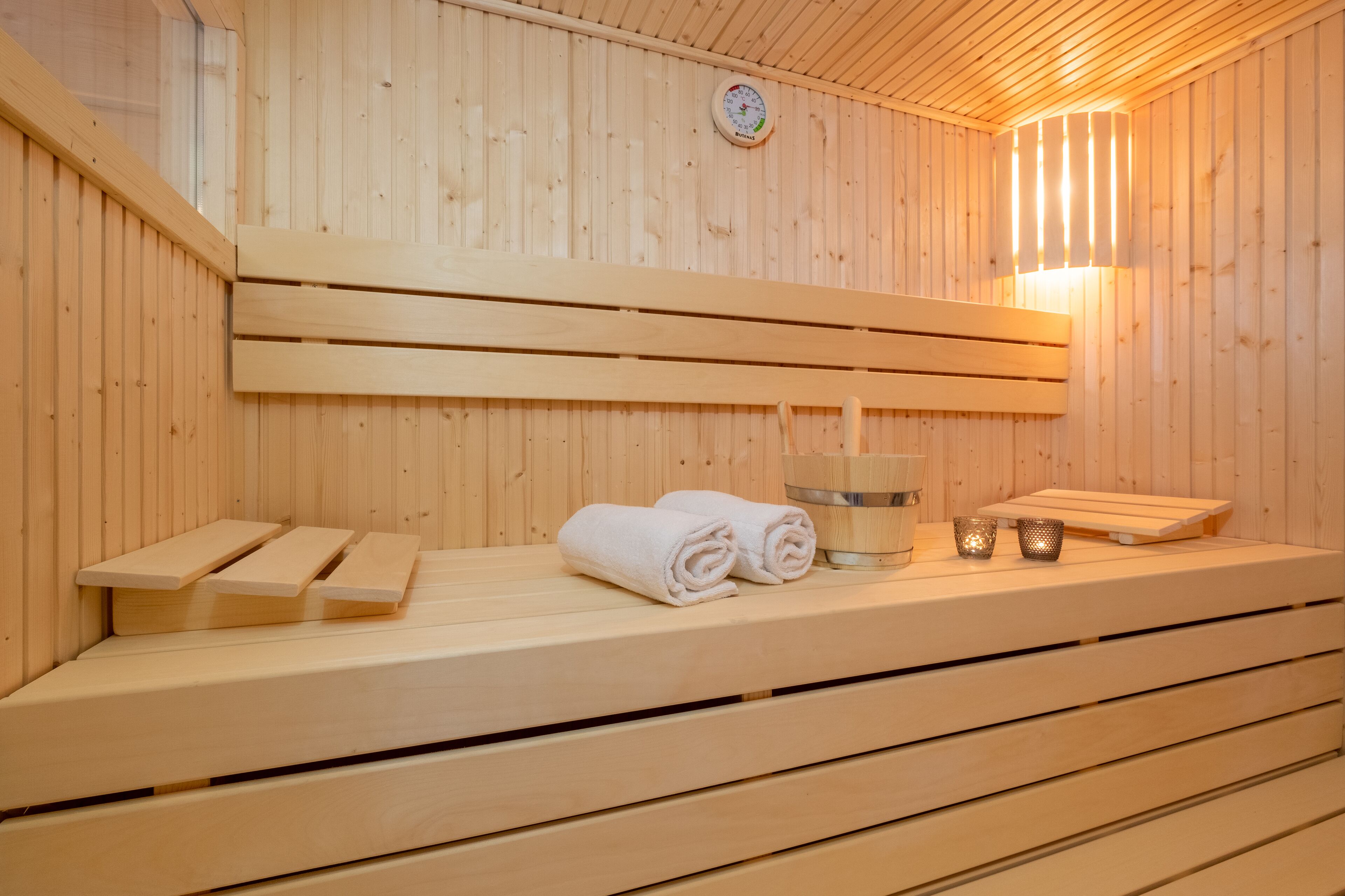 A wooden sauna with benches, towels, and a wall-mounted thermometer.