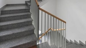 A staircase with stone steps and wooden handrails, leading to a landing with a fire extinguisher on the wall. - Romeo & Julia (Split)