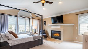 Un dormitorio con cama con dosel, chimenea, televisor montado encima y ventanas grandes con persianas.