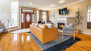 Un amplio salón con suelo de madera, un sofá de cuero, un sillón gris, una chimenea y una escalera que sube a otro nivel.