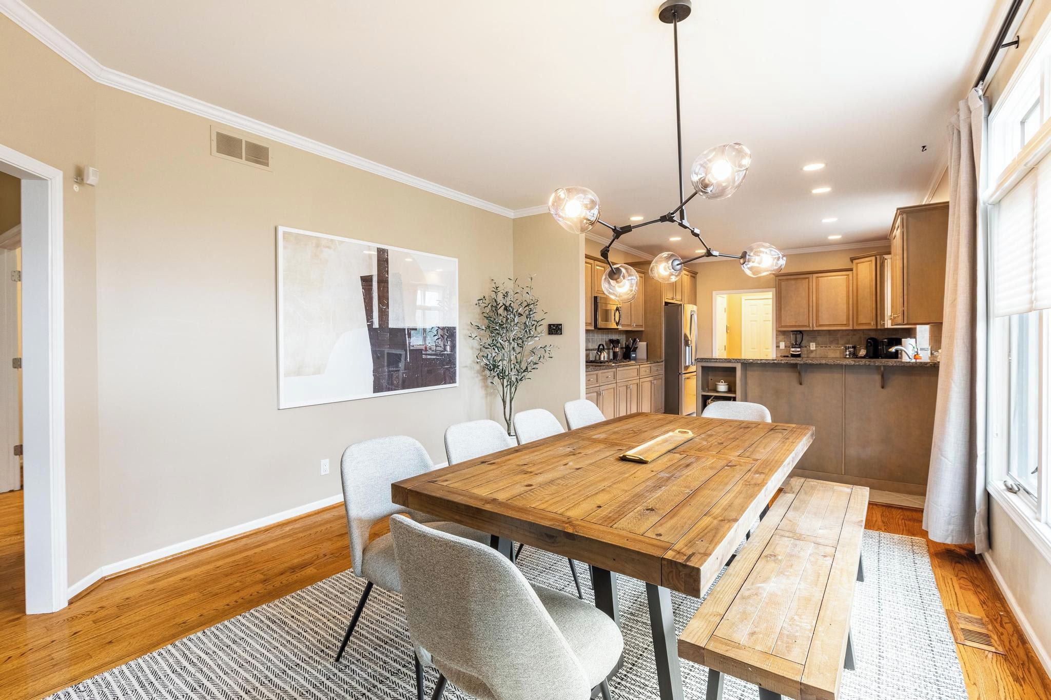 A dining area with a wooden table and chairs, a chandelier, and a view into the kitchen.