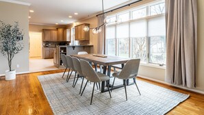 Una cocina moderna con armarios de madera, un comedor con mesa y sillas de madera, y un amplio ventanal con cortinas.