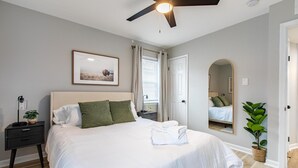 Un dormitorio ordenado con cama, mesita de noche y ventilador de techo.
