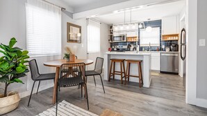 Una cuina moderna amb armaris blancs, una illa central i tamborets.