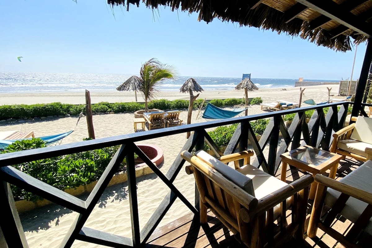 A beachside terrace with wooden furniture, a hammock, and a view of the ocean.