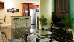 Una cocina moderna con barra, una silla de comedor, una mesa con cubierta de vidrio y un televisor de pantalla plana.