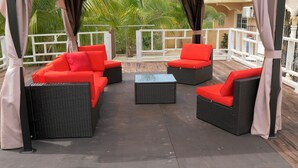 Un espacio de estar al aire libre con techo, mobiliario de mimbre y cojines rojos.