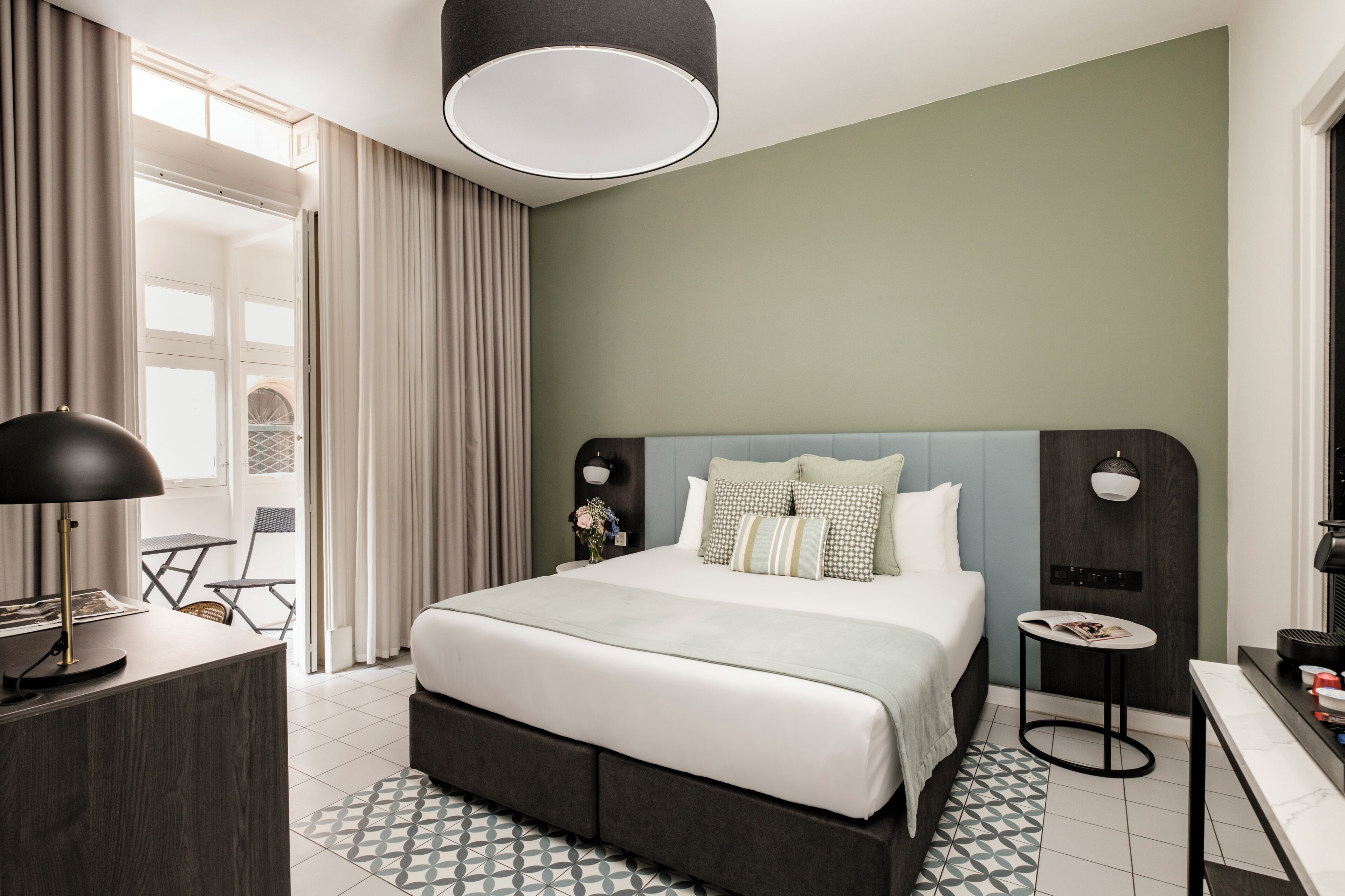 Een moderne hotelkamer met een groot bed, een bureau, een stoel, een bijzettafeltje en een lamp.