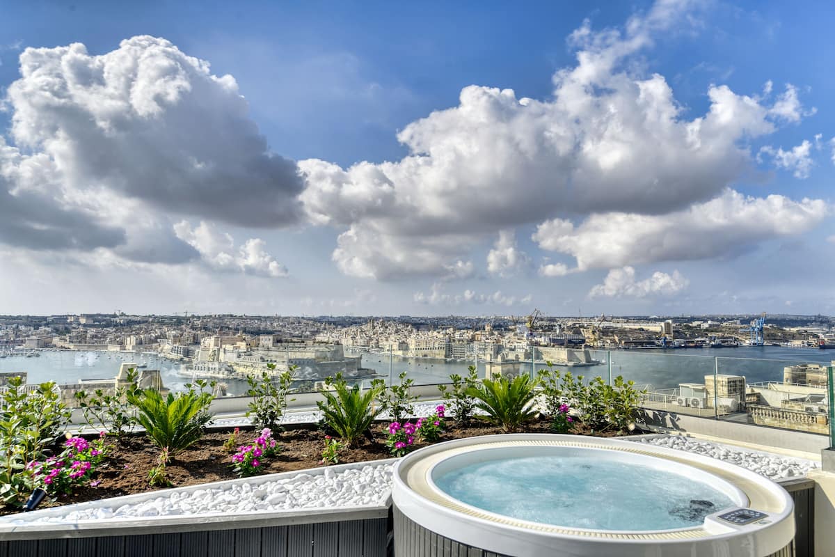 A rooftop pool with a city view, surrounded by plants and flowers.