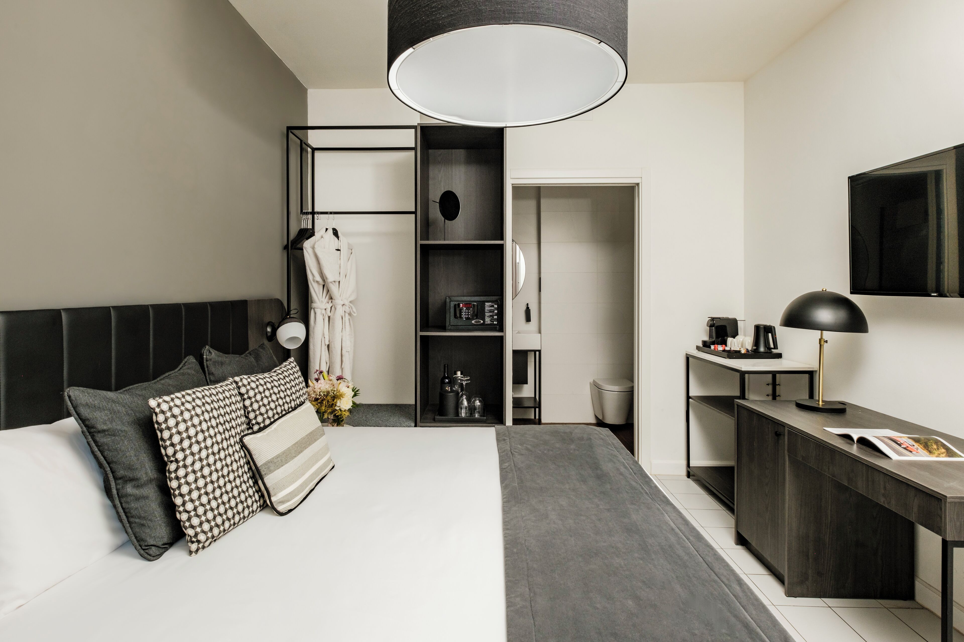 A modern hotel room with a bed, bedside table, desk, and a large mirror.
