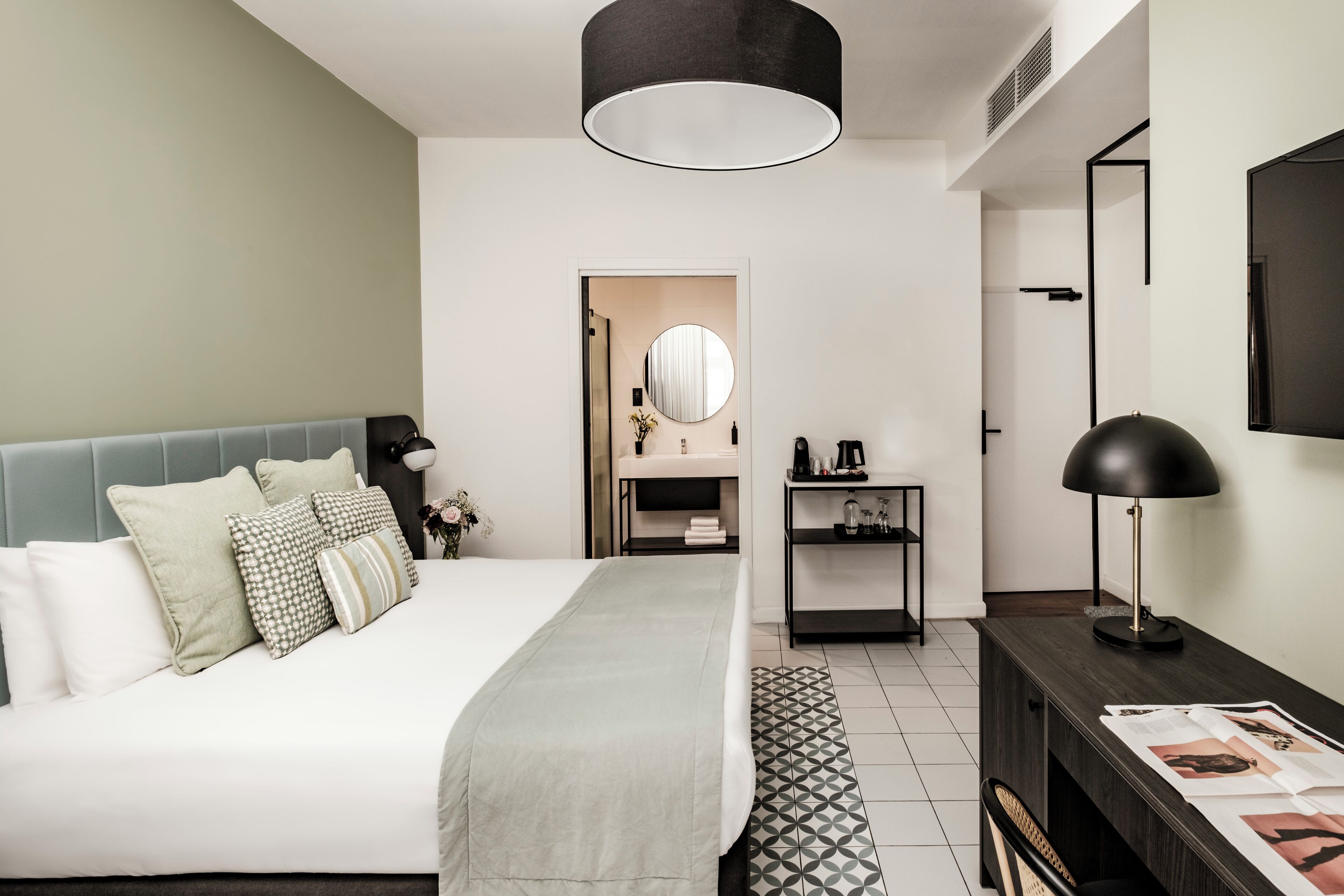 Een moderne hotelkamer met een groot bed, nachtkastje, bureau en spiegel.