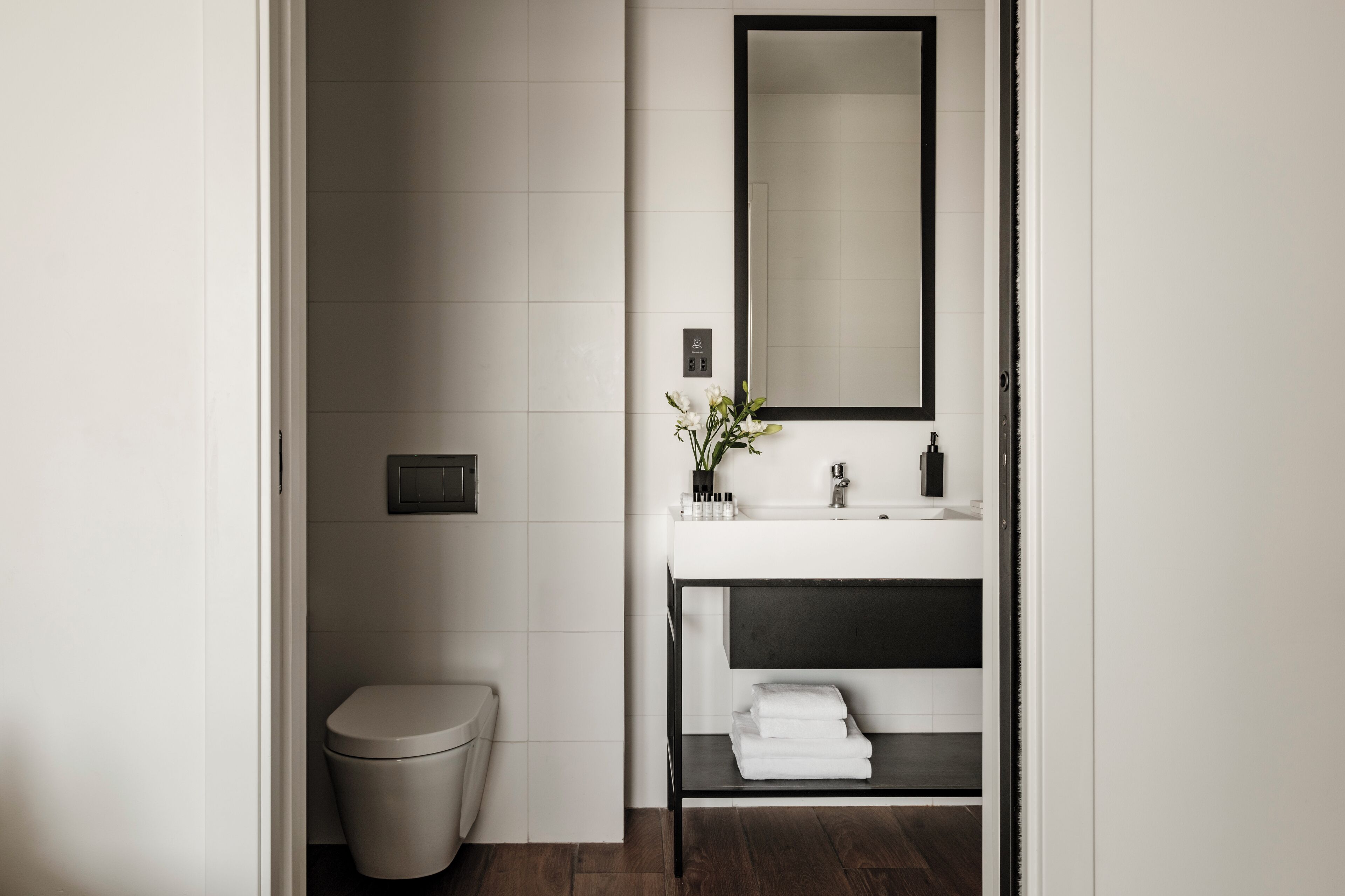 Un baño moderno con inodoro, lavabo, espejo y repisas con toallas.