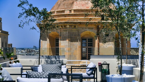 A rooftop terrace with outdoor seating, a view of the city, and a historic building in the background. - Palazzo Ignazio (Valletta)