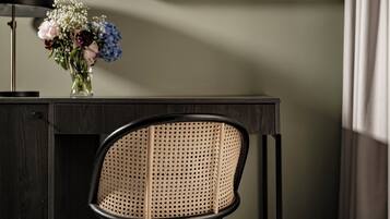 A desk with a vase of flowers, a lamp, and a chair with a woven backrest.
