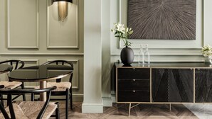 A dining area with a round table and chairs, a black cabinet with drawers, and a wall-mounted light fixture. - Palazzo Ignazio (Valletta)