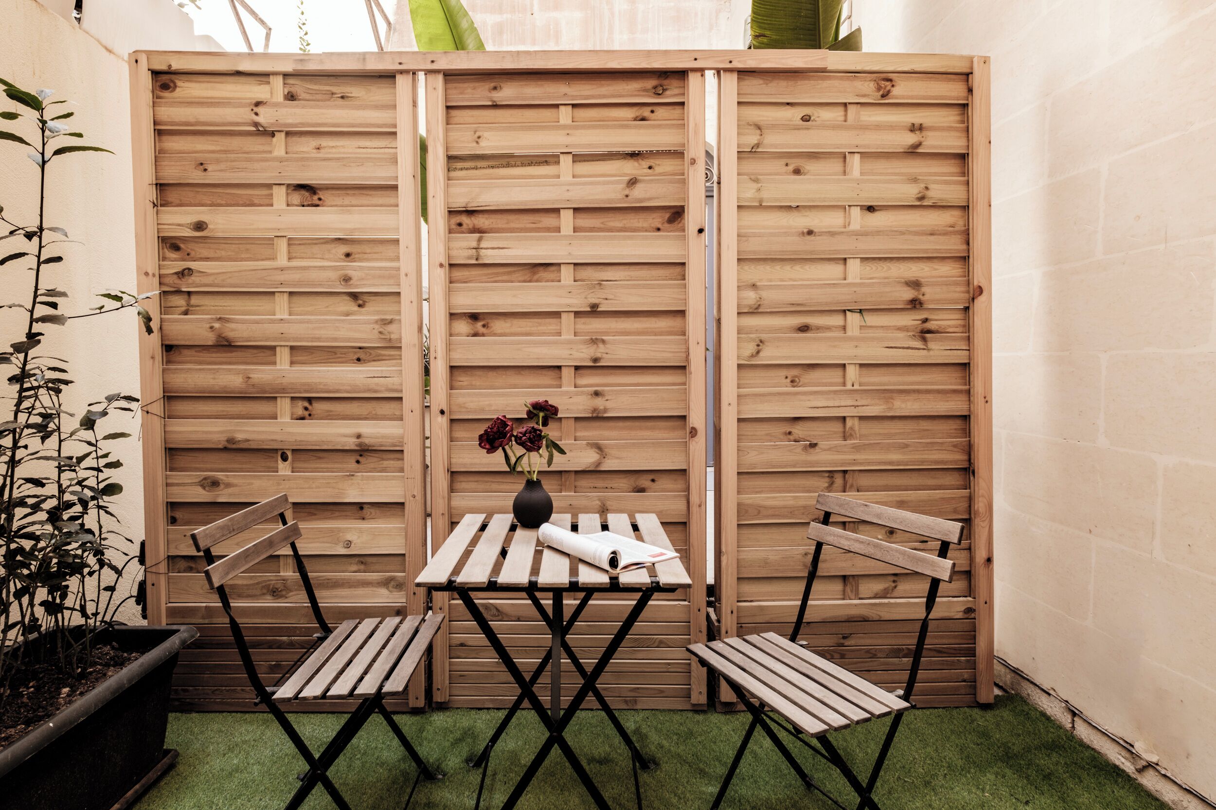 Een houten omheining met een tafel en twee stoelen in een tuin.