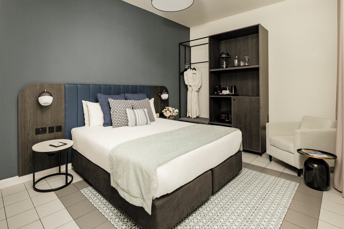 A modern bedroom with a large bed, bedside tables, a wardrobe, and a seating area.