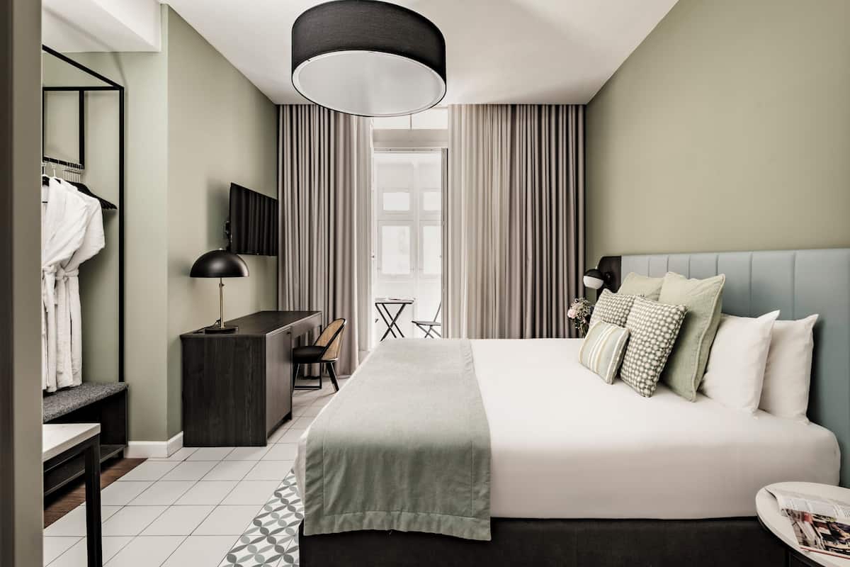A modern hotel room with a large bed, a desk, a chair, a TV, and a window with curtains.