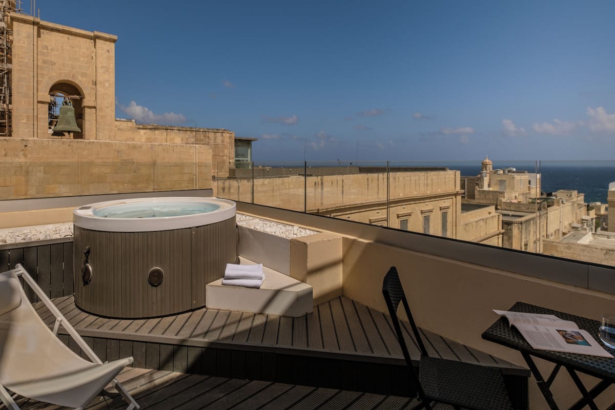 A rooftop terrace with a hot tub, lounge chairs, and a table with a newspaper.