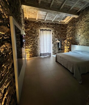 Une chambre avec un mur en pierre, un lit, une armoire et un miroir.