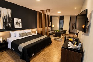 Una habitación de hotel moderna con una cama grande, un escritorio con computadora, una silla y un televisor.