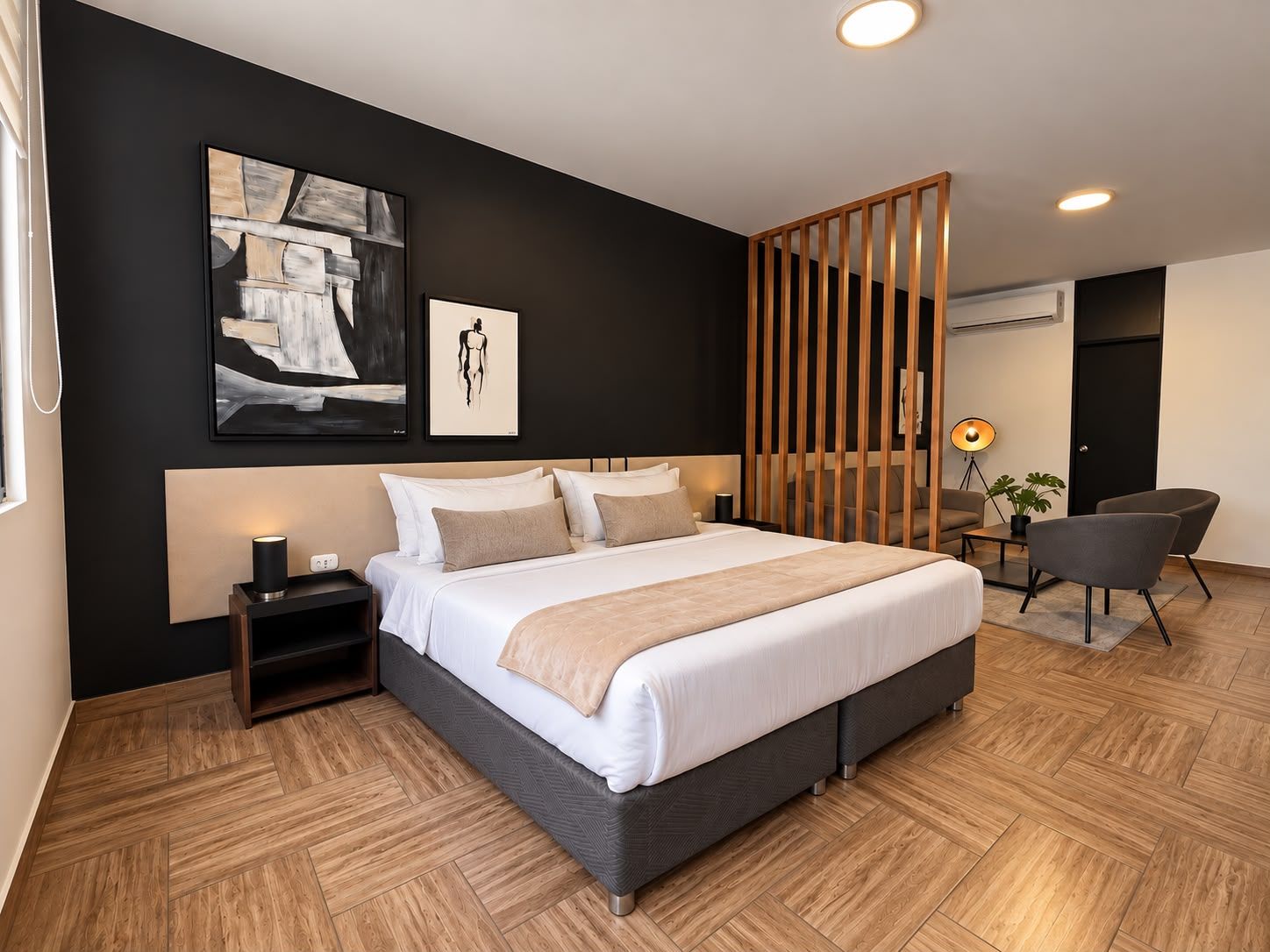 Habitación de hotel moderna con una cama grande, una mesita de noche, un escritorio con silla y un ventanal amplio.