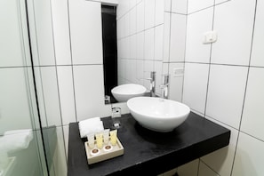 Un baño moderno con dos lavamanos blancos, una encimera negra y una cabina de ducha de vidrio.