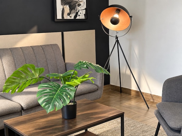 Una sala de estar moderna con un sofá gris, una mesa de centro de madera, una planta en maceta y una lámpara de pie.