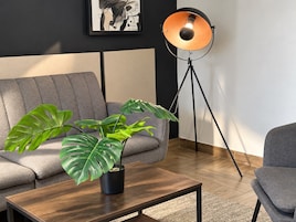 Una sala de estar moderna con un sofá gris, una mesa de centro de madera, una planta en maceta y una lámpara de pie.