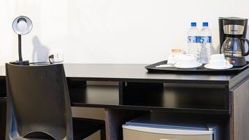 Habitación de hotel con escritorio, silla, cafetera, botellas de agua y refrigerador.