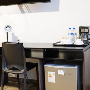 Habitación de hotel con escritorio, silla, cafetera, botellas de agua y refrigerador.