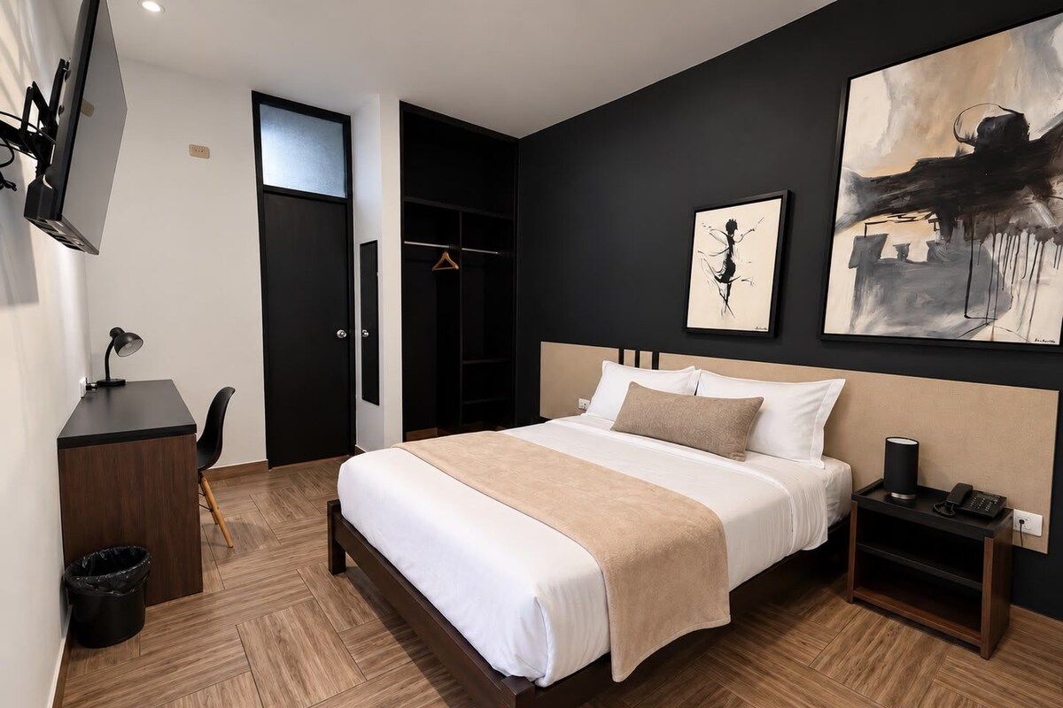 Una habitación de hotel moderna con una cama grande, un escritorio, una silla, un armario y obras de arte en las paredes.