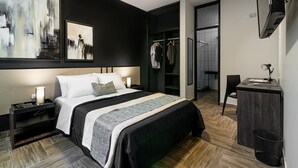 A modern hotel room with a large bed, a desk, a wardrobe, and a TV mounted on the wall.