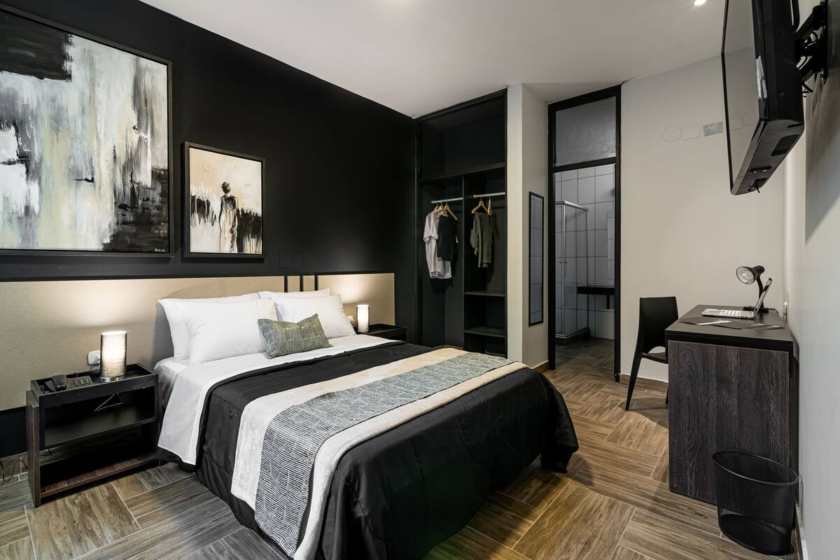 A modern hotel room with a large bed, a desk, a wardrobe, and a TV mounted on the wall.