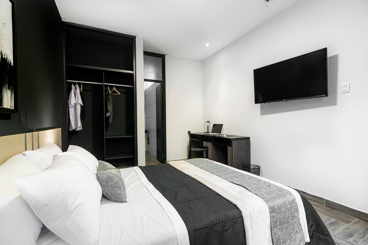 A modern hotel room with a bed, a desk, a TV, and a walk-in closet.