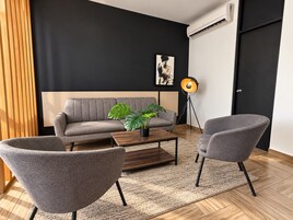 Una sala de estar moderna con un sofá gris, dos sillones, una mesa de centro, una planta en maceta, una lámpara de pie y un cuadro en la pared.