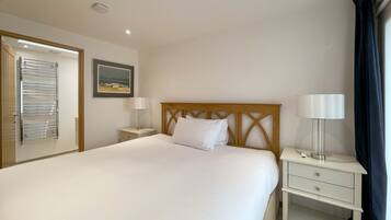 A neatly arranged hotel room with a large bed, a wooden headboard, a bedside table with a lamp, and a wall-mounted towel rack.