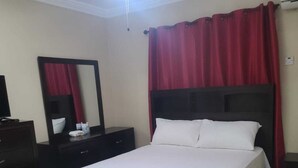 Hotellihuone, jossa on sänky, lipasto, peili ja punainen verho.