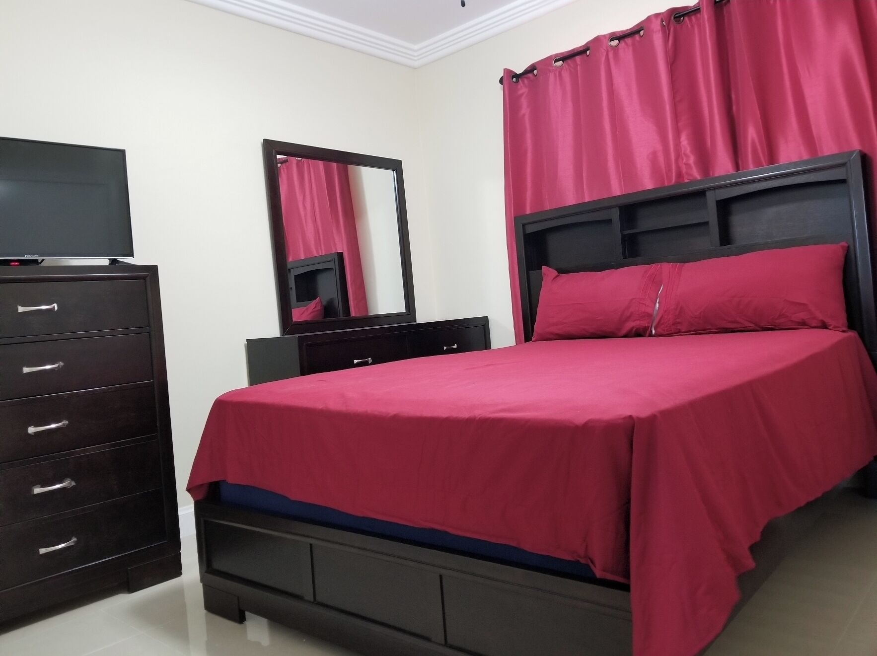 A bedroom with a bed, a dresser, a mirror, and a television.