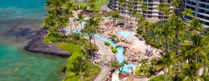 Um resort com área de piscina, palmeiras e vista para o oceano.