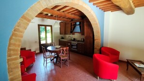 Un comedor con una mesa redonda y sillas, una cocina con armarios de madera y un salpicadero de azulejos, y una silla roja en un rincón.